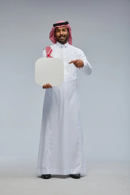 رجل سعودي مبتسم بزي تقليدي يحمل لوحة إعلانية بيضاء فارغة
