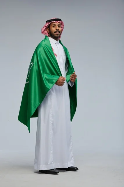 رجل سعودي يحمل علم المملكة بالزي التقليدي