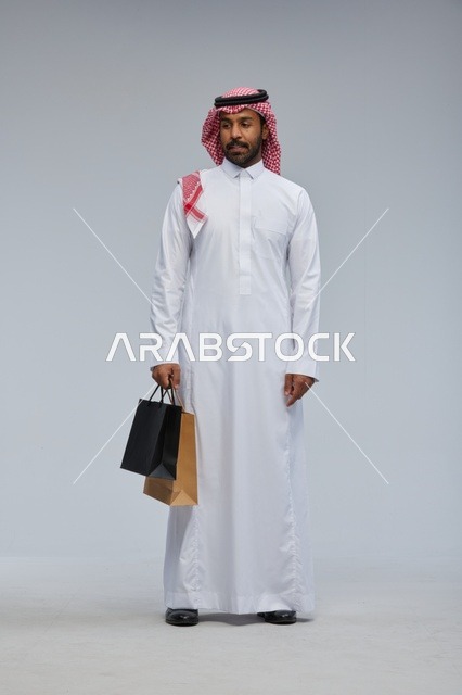 رجل سعودي بالزي التقليدي يحمل أكياس تسوق