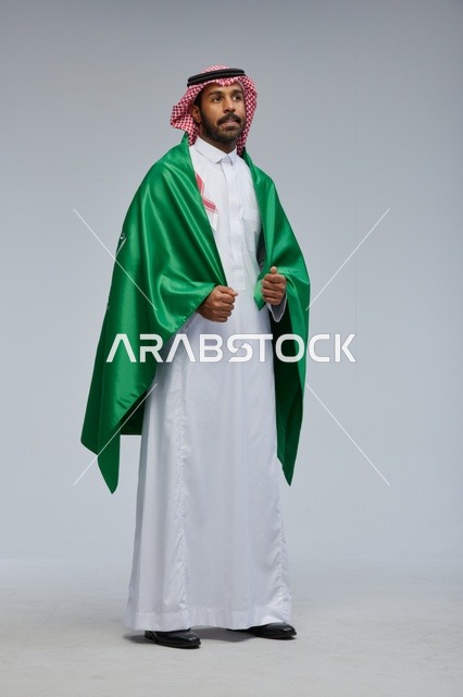 رجل سعودي بالزي التقليدي يحمل علم المملكة العربية السعودية