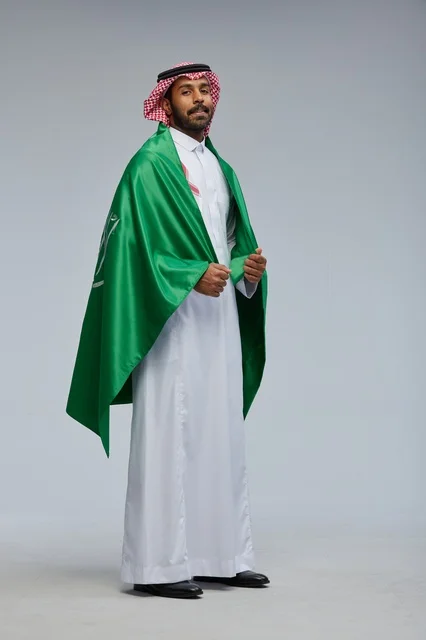 رجل سعودي بالزي التقليدي مع علم المملكة العربية السعودية
