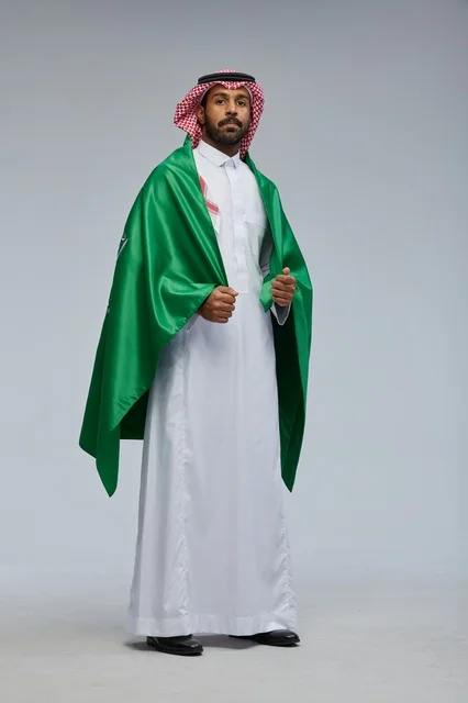 رجل سعودي بالعلم الوطني يرتدي الثوب التقليدي