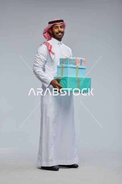 رجل سعودي يحمل علب هدايا بخلفية رمادية