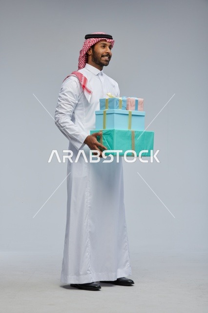 رجل سعودي يحمل صناديق هدايا على خلفية رمادية