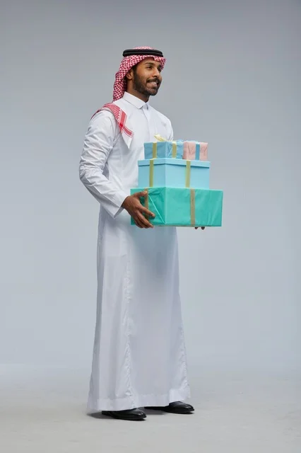 رجل سعودي يحمل صناديق هدايا على خلفية رمادية