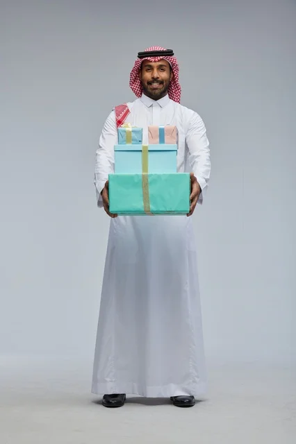 رجل سعودي يحمل علب هدايا أمام خلفية رمادية