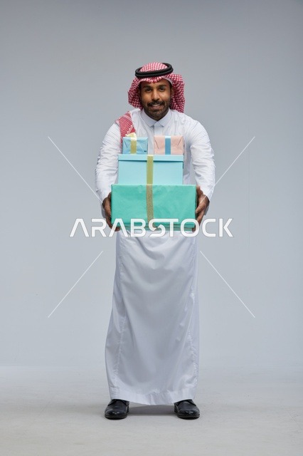 رجل سعودي يحمل صناديق هدايا بخلفية رمادية