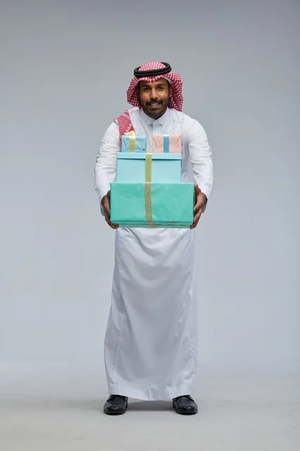 رجل سعودي يحمل صناديق هدايا بخلفية رمادية