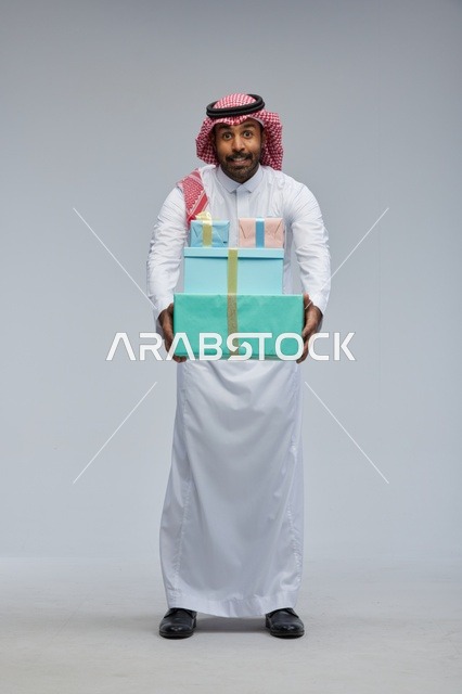 رجل سعودي يحمل علب هدايا بخلفية رمادية