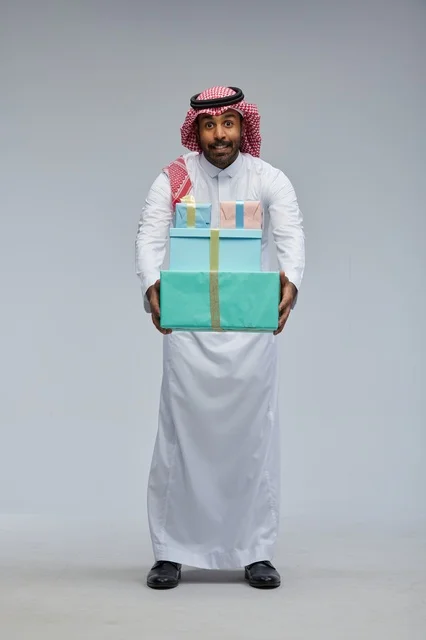 رجل سعودي يحمل علب هدايا بخلفية رمادية