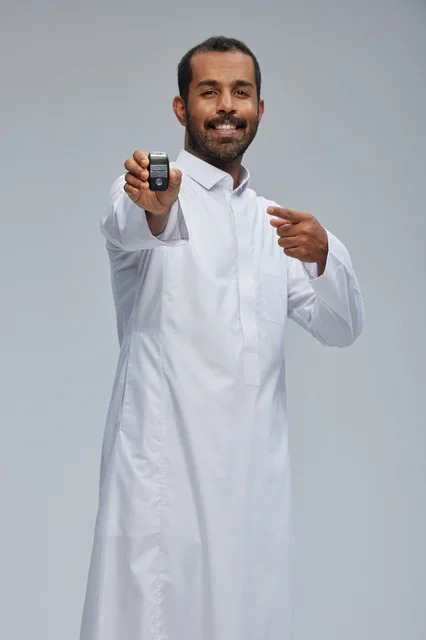رجل سعودي يحمل مفتاح سيارة بخلفية رمادية