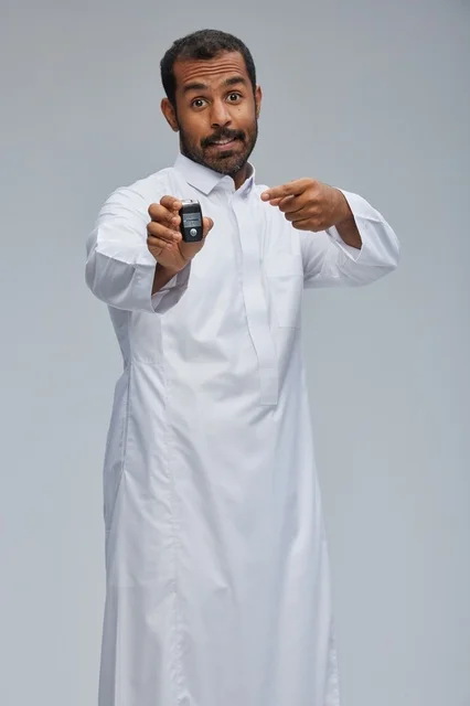 رجل سعودي بالثوب يحمل مفتاح سيارة بخلفية رمادية