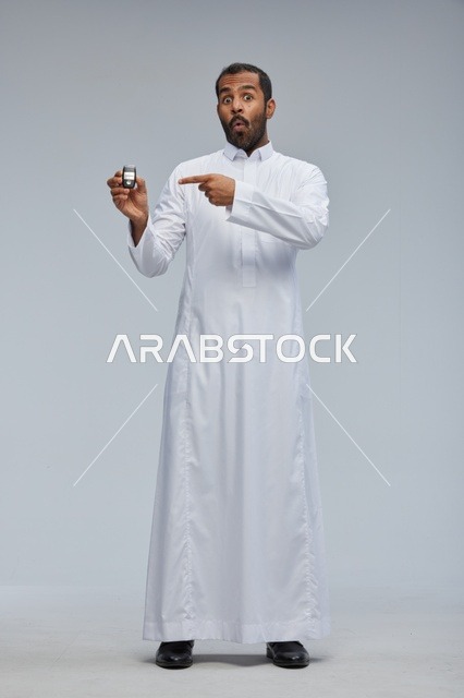 رجل سعودي يحمل مفتاح سيارة بتعبير متفاجئ في استوديو