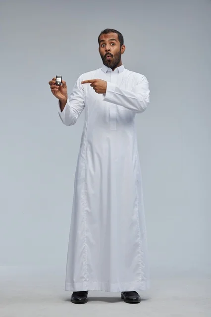 رجل سعودي يحمل مفتاح سيارة بتعبير متفاجئ في استوديو