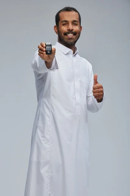 رجل سعودي يرتدي الثوب يحمل مفتاح سيارة مع إشارة الإبهام
