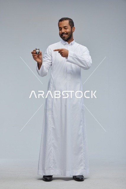 رجل سعودي يحمل مفتاح سيارة أمام خلفية رمادية