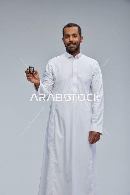 رجل سعودي يمسك مفتاح سيارة مبتسم في خلفية استوديو