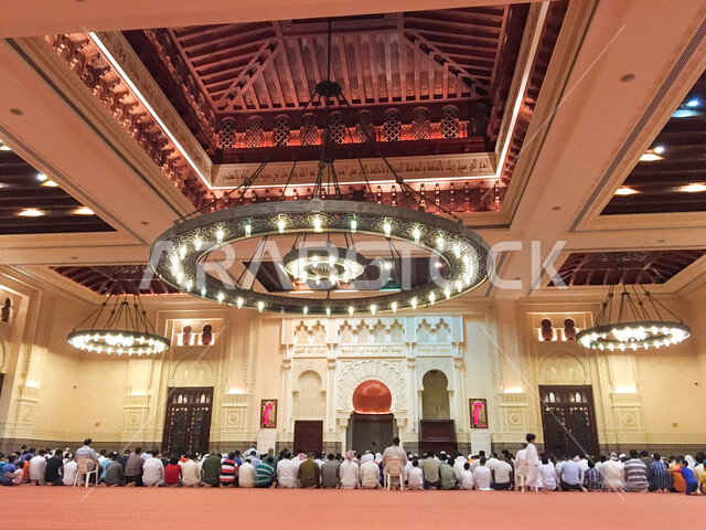 صورة من الخلف لمجموعة من المصلين يؤدون الصلاة في مسجد بن حمودة بمدينة العين بإمارة أبو ظبي بدولة الإمارات العربية المتحدة ، أجواء رمضان المبارك ، ثرية عملاقة ، الزخرفة الإسلامية ، العبادة والتقرب إلى الله