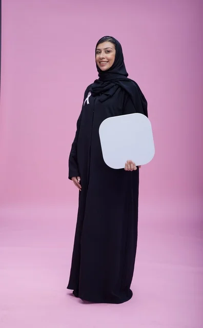امرأة سعودية تحمل شريط وردي ولوحة فارغة للتوعية