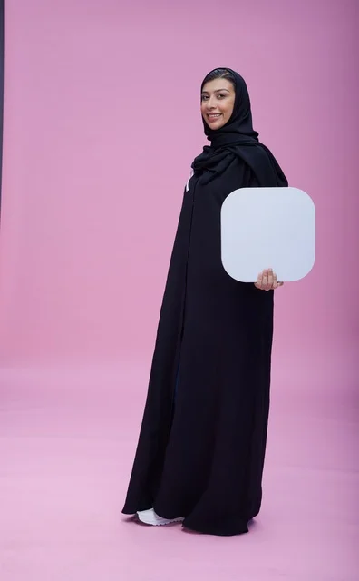 امرأة سعودية تحمل لوحة بيضاء فارغة خلفية وردية