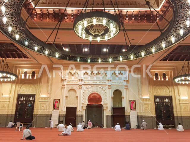 صورة من الخلف لمجموعة من المصلين يؤدون الصلاة في مسجد بن حمودة بمدينة العين بإمارة أبو ظبي بدولة الإمارات العربية المتحدة ، أجواء رمضان المبارك ، ثرية عملاقة ، الزخرفة الإسلامية ، العبادة والتقرب إلى الله