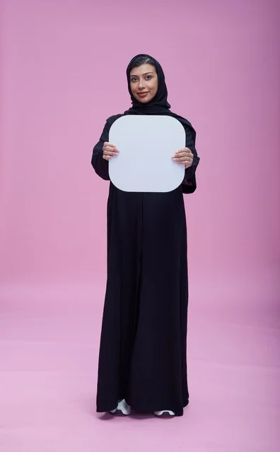 امرأة سعودية تحمل لوحة بيضاء فارغة بخلفية وردية