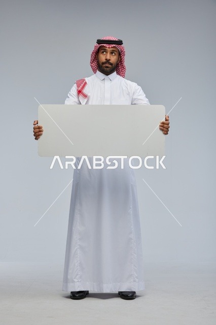 رجل سعودي يحمل لوحة بيضاء فارغة في الاستوديو