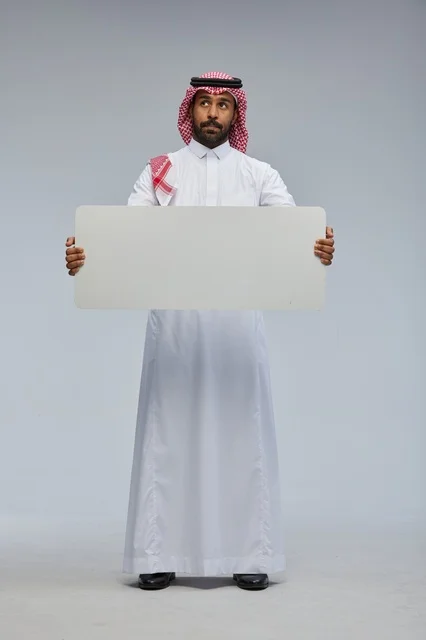 رجل سعودي يحمل لوحة بيضاء فارغة في الاستوديو