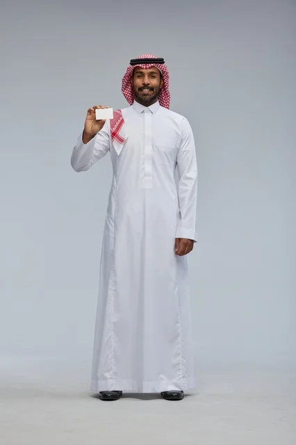 رجل سعودي يحمل بطاقة عمل فارغة بخلفية رمادية