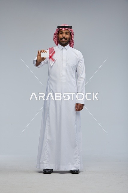 رجل سعودي يحمل بطاقة عمل فارغة بخلفية رمادية