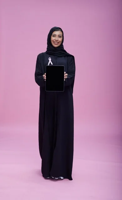 امرأة سعودية تحمل جهازاً لوحياً مع شريط سرطان الثدي