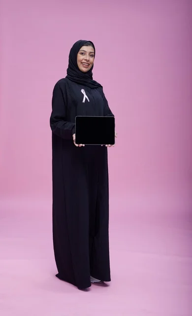 Saudi Woman Holding Tablet with Breast Cancer Ribbon