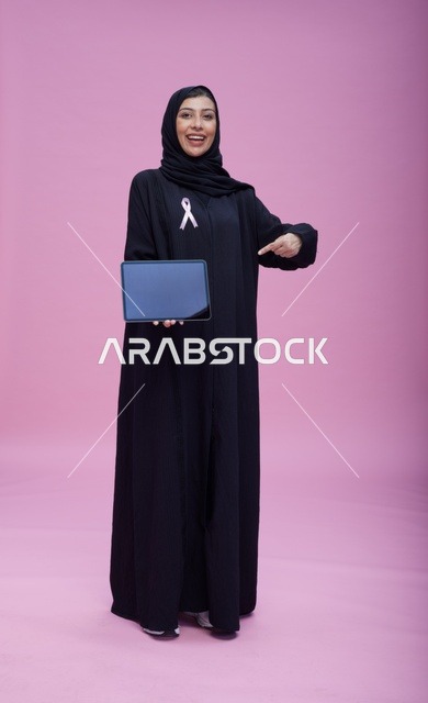 امرأة سعودية مع جهاز لوحي وشعار سرطان الثدي