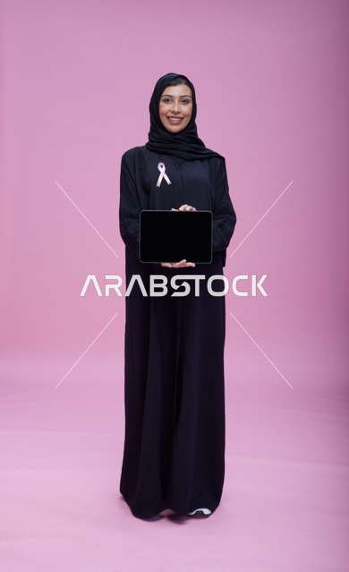 امرأة سعودية تحمل جهازاً لوحياً للتوعية بسرطان الثدي