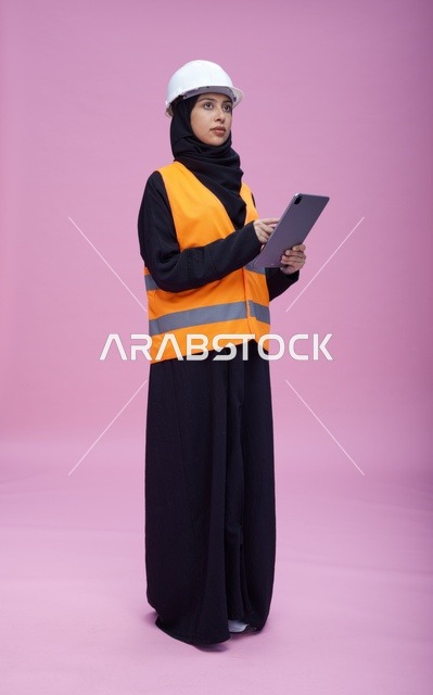مهندسة سعودية تحمل جهاز لوحي في استوديو بخلفية وردية