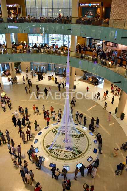 صورة من أعلى لمجموعة من السياح داخل دبي مول بإمارة دبي، السياحة في الإمارات العربية المتحدة ، مول دبي، مراكز التسوق ، مجسم "برج خور دبي" المستقبلي في قاعة جراند أتريوم بدبي مول، معلم معماري جديد، مجسم ضخم لبرج خور دبي