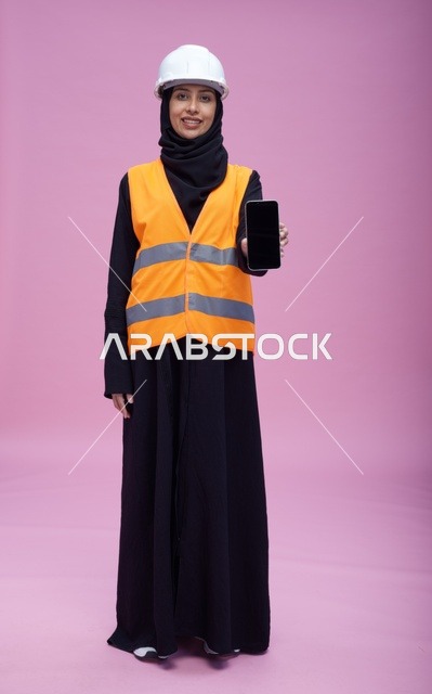 مهندسة سعودية تحمل هاتف ذكي أمام خلفية وردية