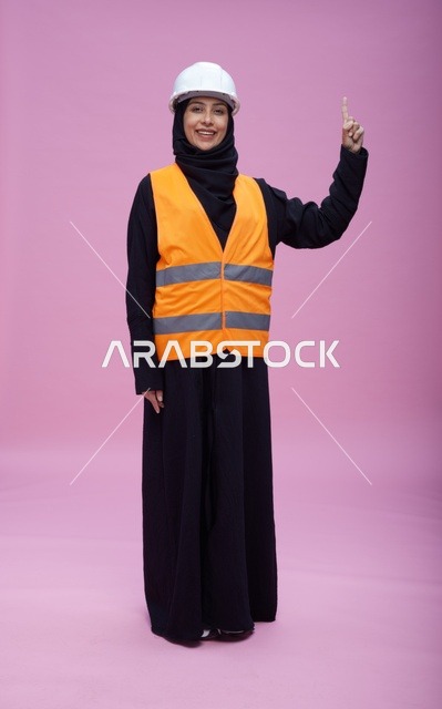 مهندسة سعودية بملابس السلامة تشير للأعلى خلفية وردية