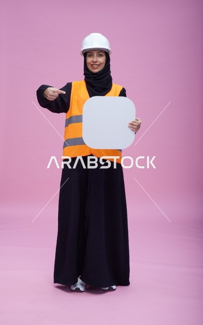مهندسة سعودية تحمل لوحة بيضاء فارغة أمام خلفية وردية