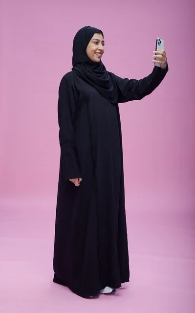 امرأة سعودية بالعباءة تلتقط صورة سيلفي بخلفية وردية