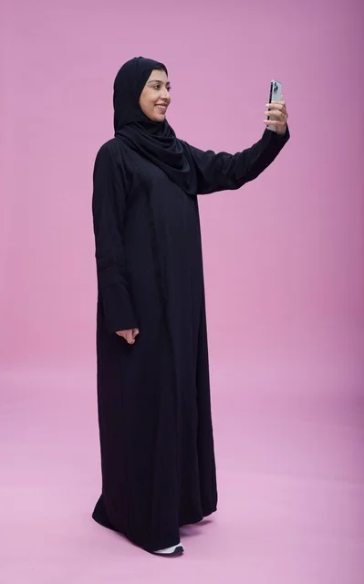امرأة سعودية بالعباءة تلتقط سيلفي على خلفية وردية