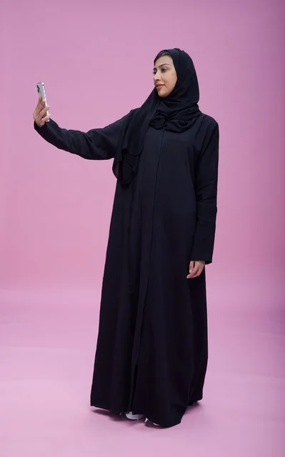 امرأة سعودية تلتقط سيلفي بالهاتف على خلفية وردية