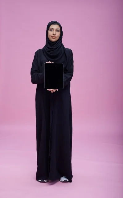امرأة سعودية تحمل جهاز لوحي بشاشة فارغة خلفية وردية