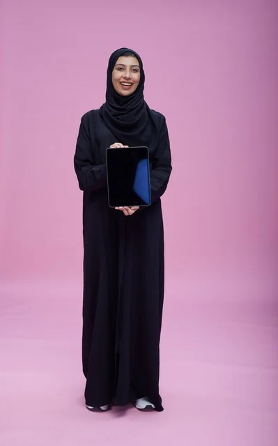 امرأة سعودية تحمل جهازاً لوحياً أمام خلفية وردية