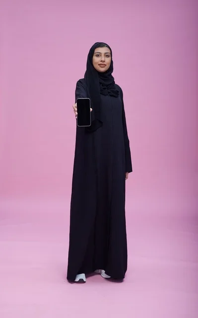 امرأة سعودية بالعباءة تحمل هاتف ذكي بشاشة فارغة