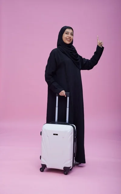 امرأة سعودية بالعباءة مع حقيبة سفر بخلفية وردية امرأة سعودية بالعباءة مع حقيبة سفر بخلفية وردية