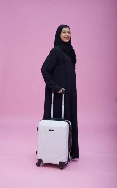 امرأة سعودية بالعباءة تقف مع حقيبة سفر