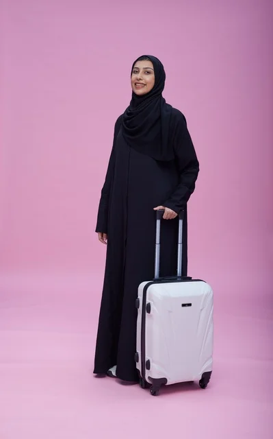 امرأة سعودية بالعباءة مع حقيبة سفر بخلفية وردية
