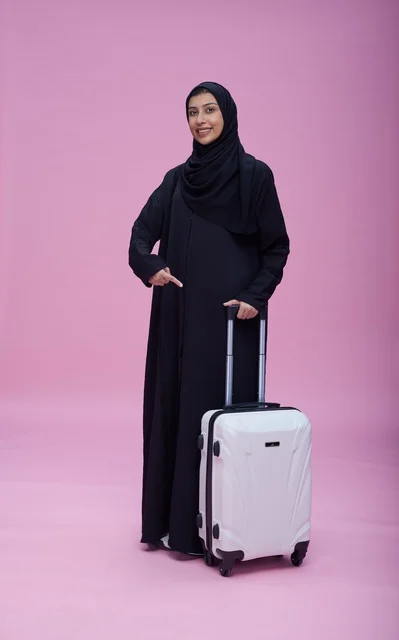 امرأة سعودية مع حقيبة سفر بخلفية وردية