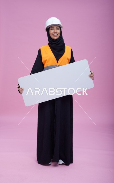 مهندسة سعودية تمسك بلوحة عرض فارغة بخلفية وردية